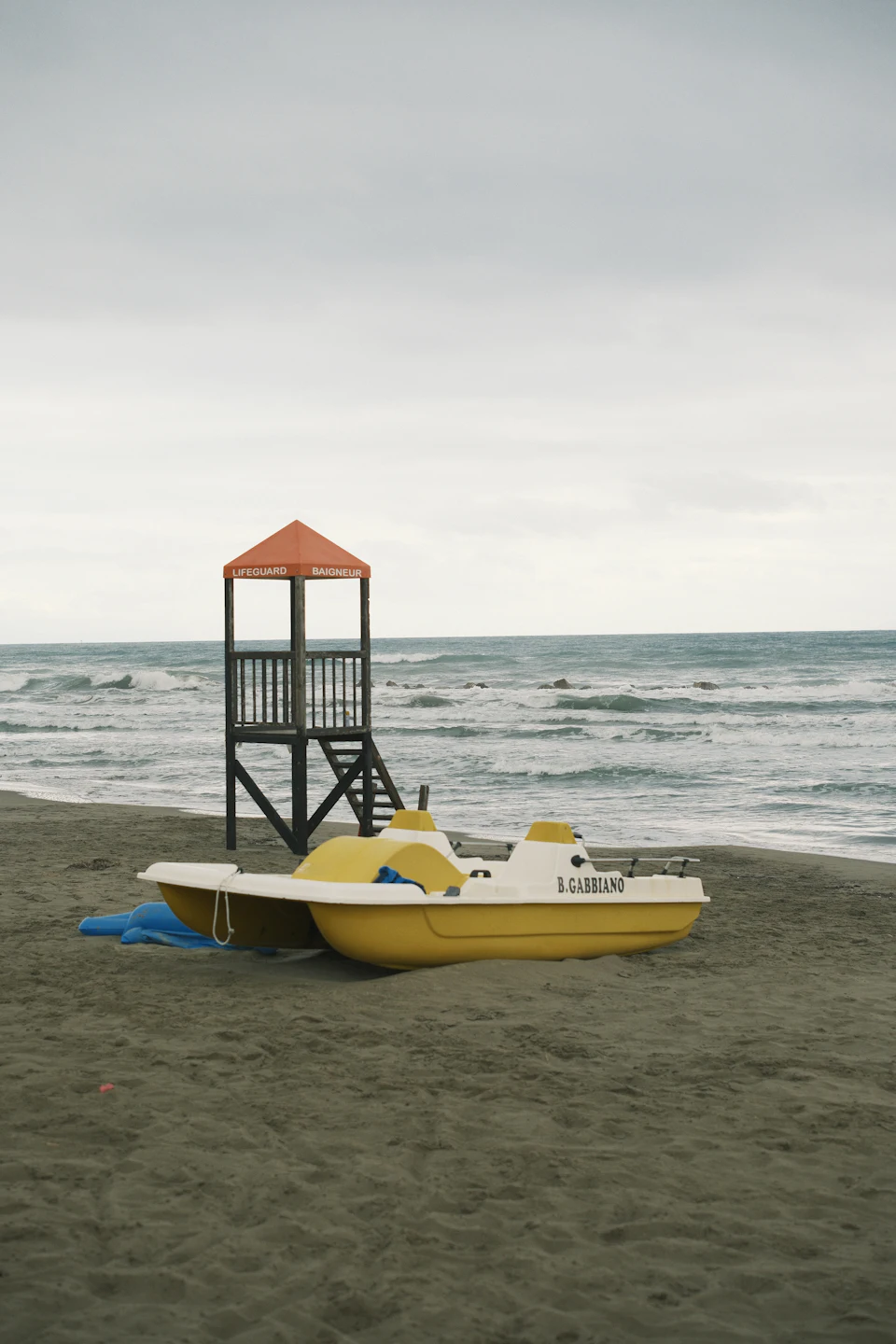 Reddingspost en gele waterfiets op een donker zandstrand, grijze zee