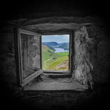 A window in a stone wall with a view of a lake
