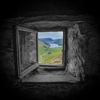 A window in a stone wall with a view of a lake