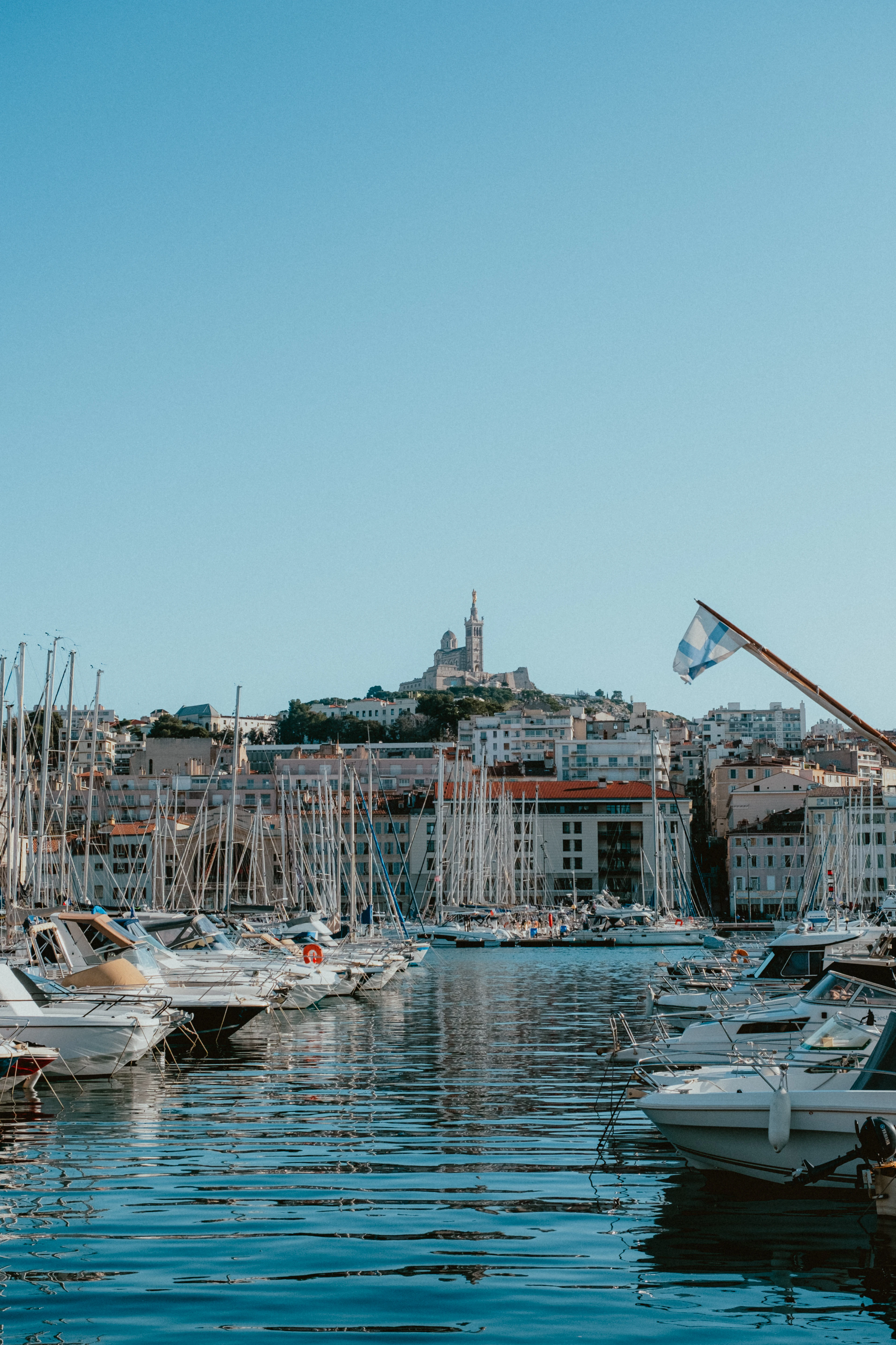 The Vieux-Port of Marseille packed with white pleasure boats and a forest of masts, the city rising behind and Notre-Dame de la Garde small on the hill under a clear blue sky