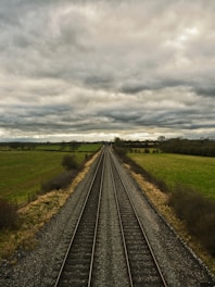 A train track running through a field under a cloudy sky