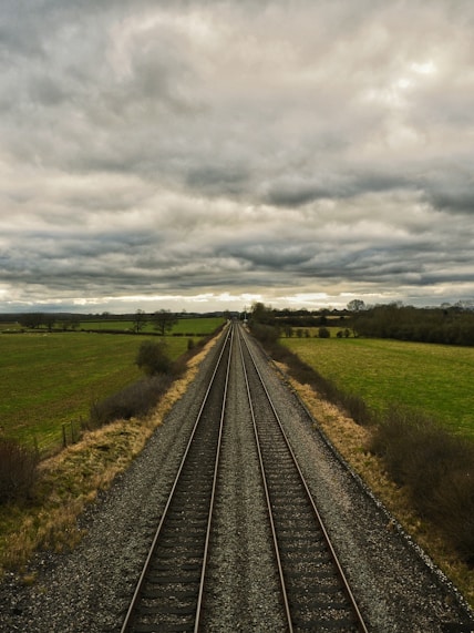 A train track running through a field under a cloudy sky