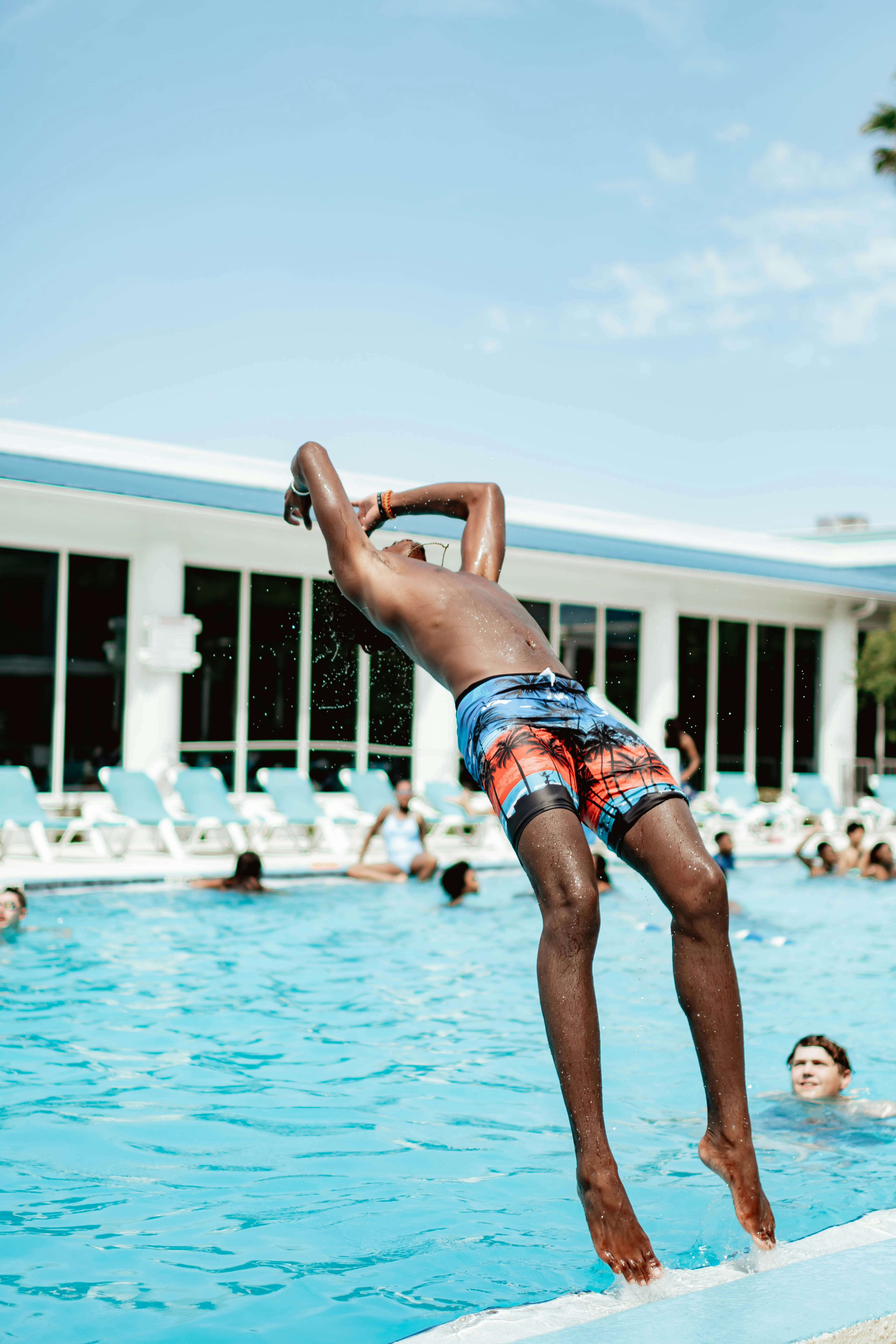 A man jumping into a swimming pool with people in the background