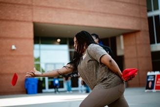 A woman is throwing a frisbee in front of a building