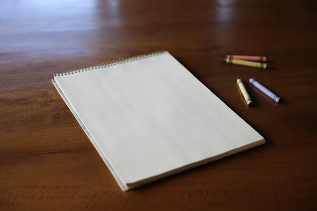 A sketchbook and crayons on a wooden table