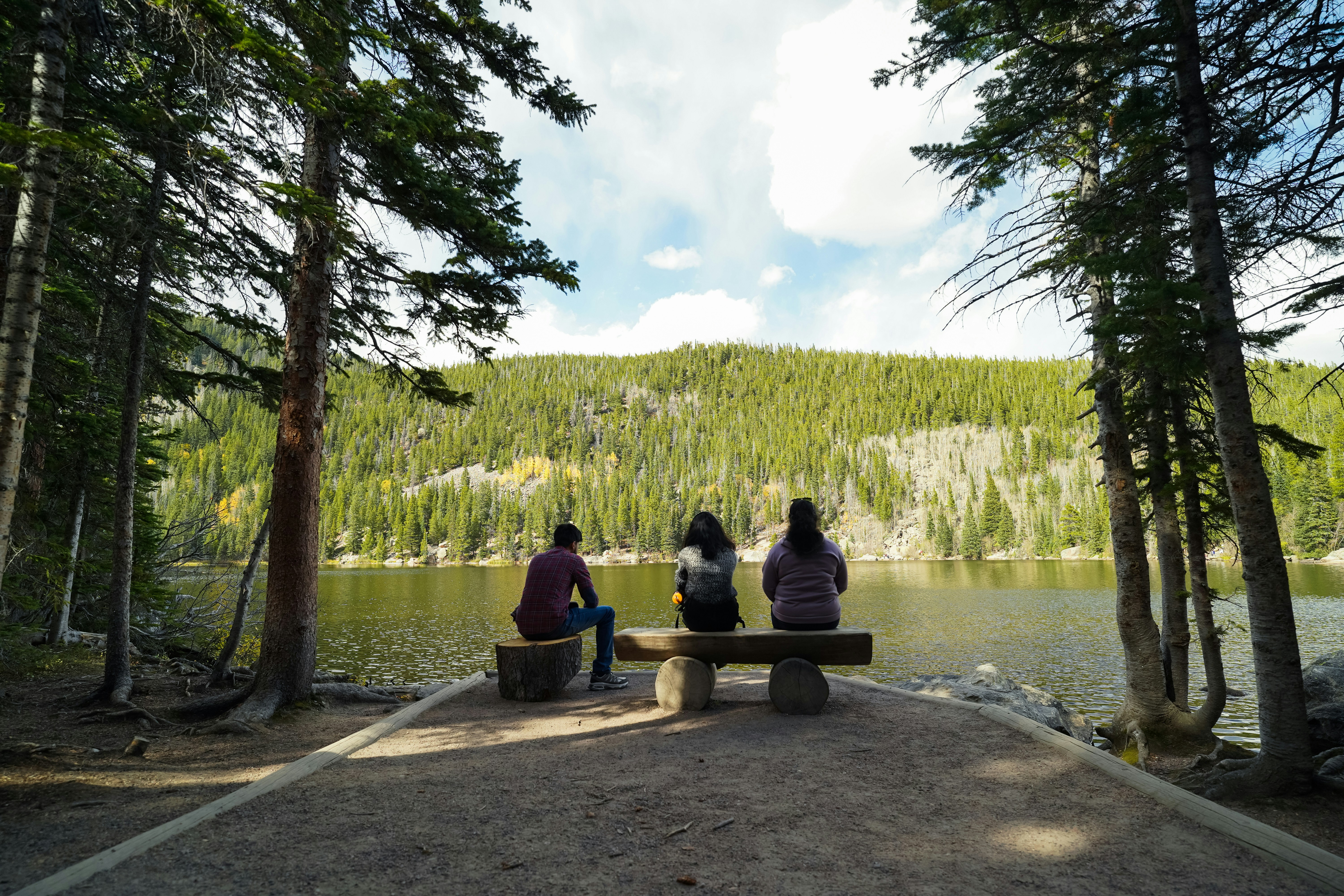 Three people sitting on a bench near a lake