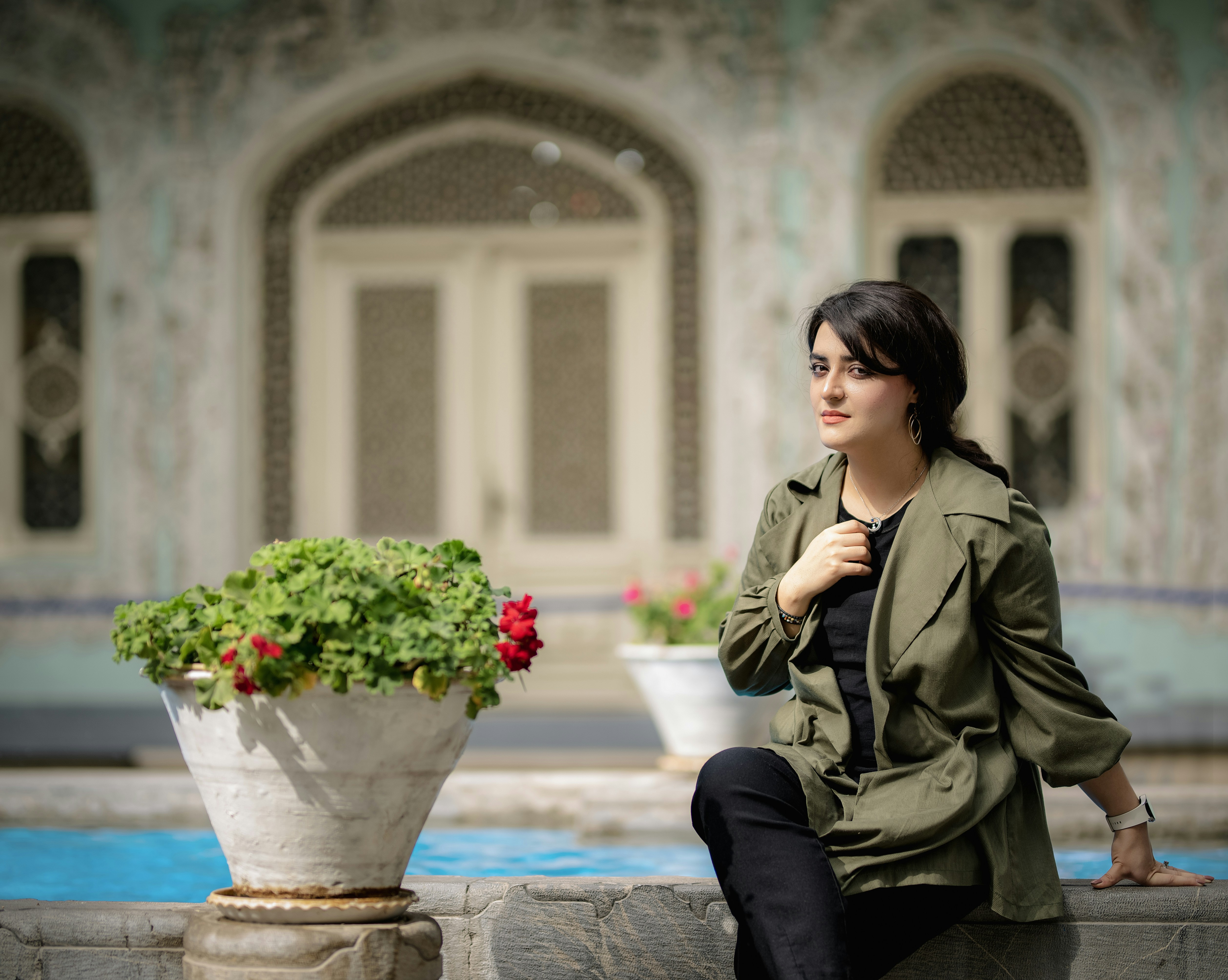A woman sitting on a wall next to a potted plant