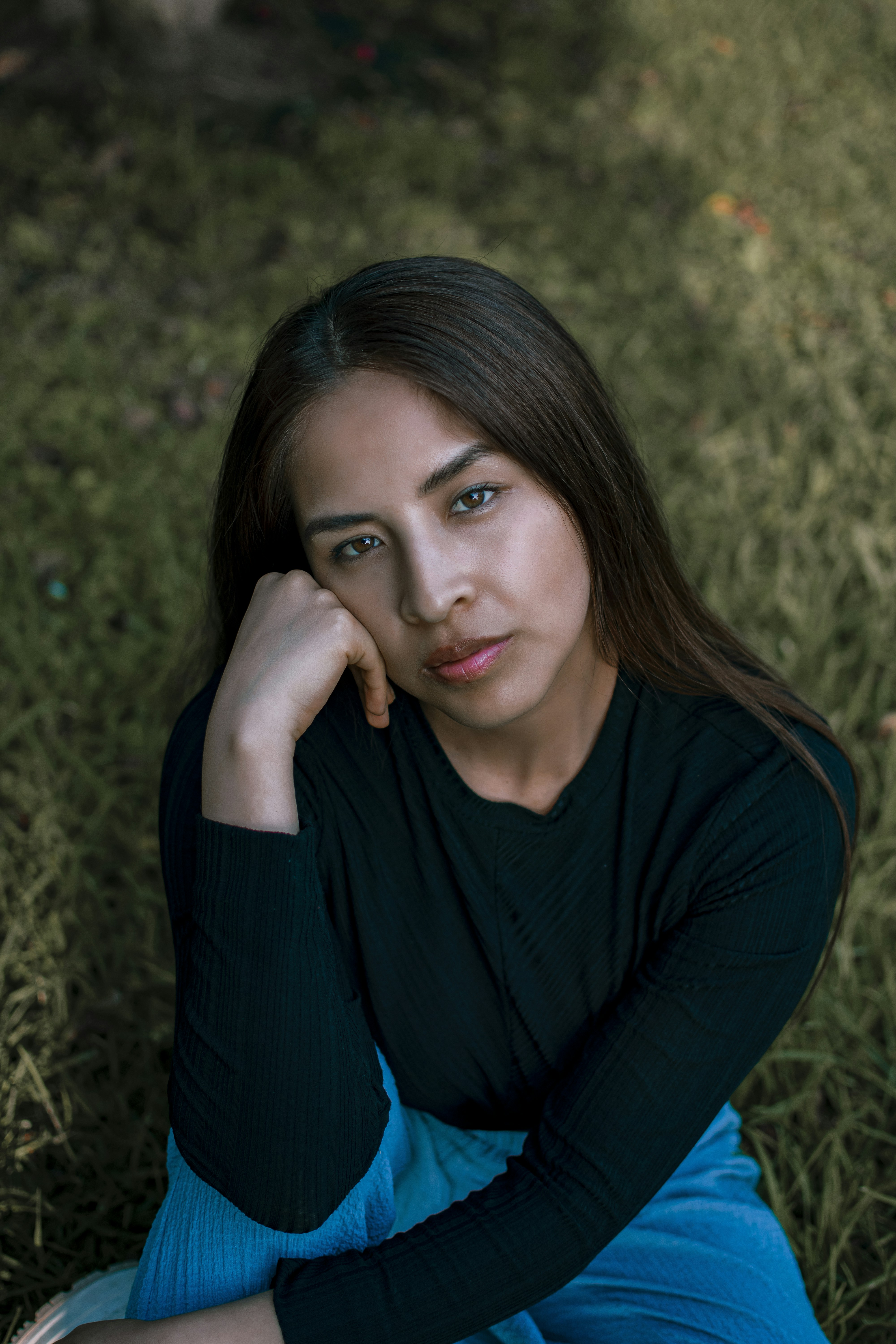 A woman sitting in the grass with her hand on her chin photo – Free ...