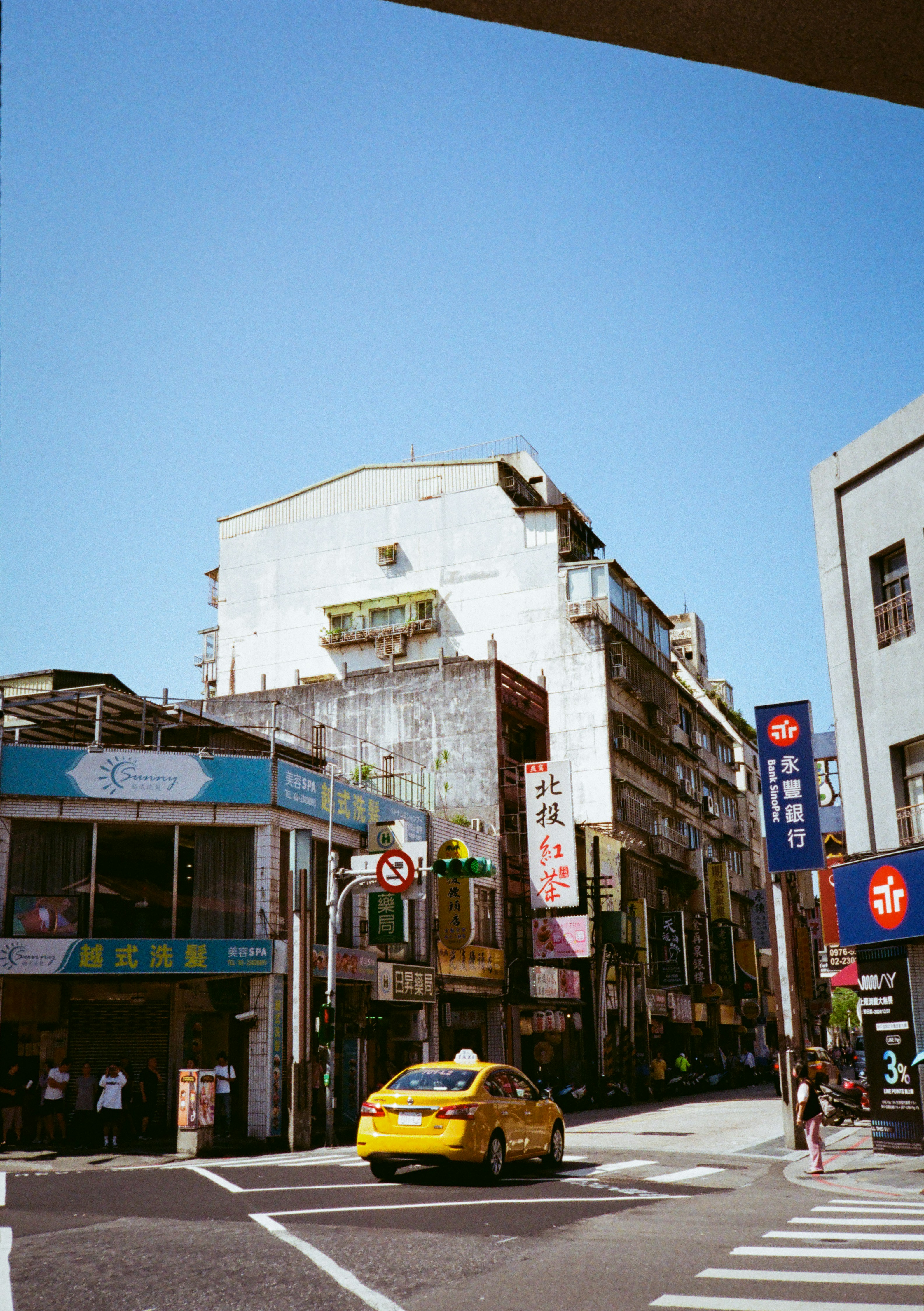A yellow car driving down a street next to tall buildings