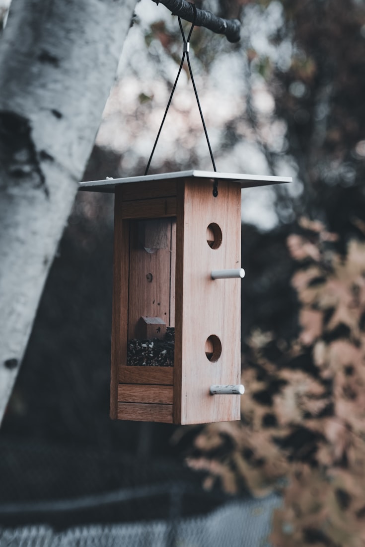 A clean, minimalist cedar tower-form birdhouse hanging outdoors.