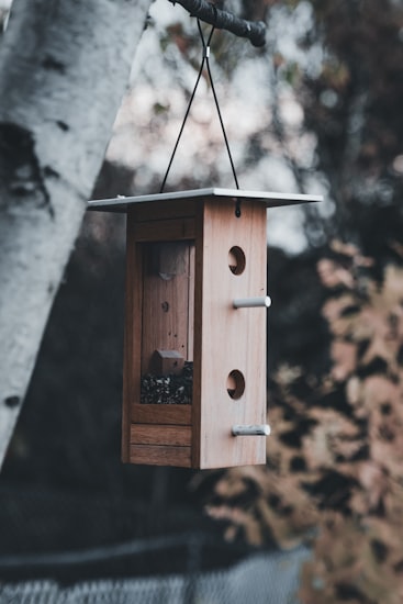 A clean, minimalist cedar tower-form birdhouse hanging outdoors.