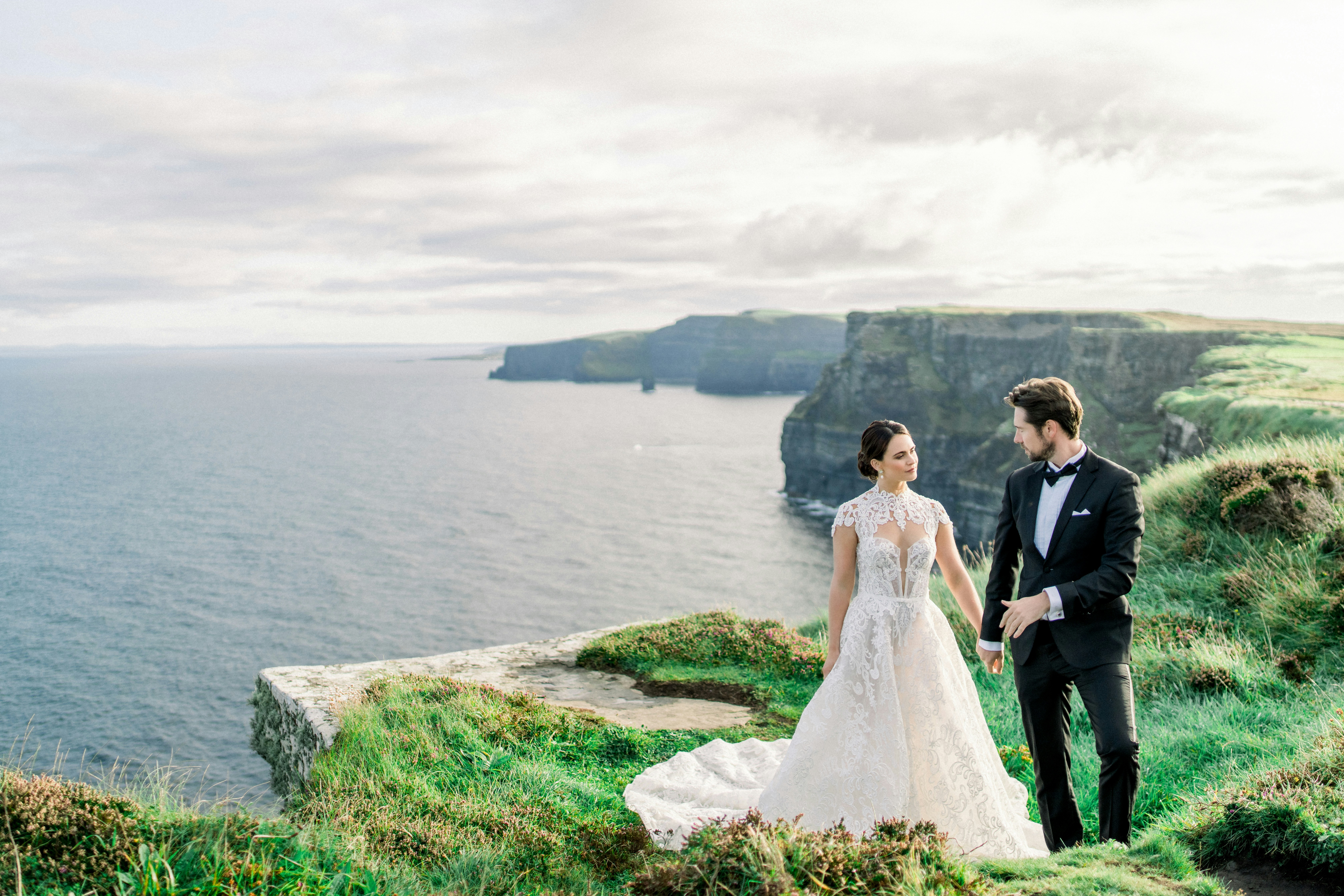 Bride and groom holding hands on a cliff overlooking the ocean.