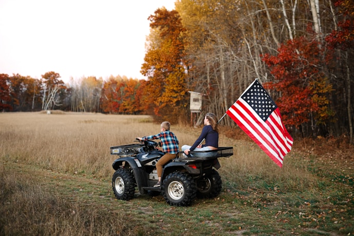 Two people on four wheelers with an american flag