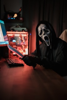 A person wearing a mask and holding a knife in front of a laptop