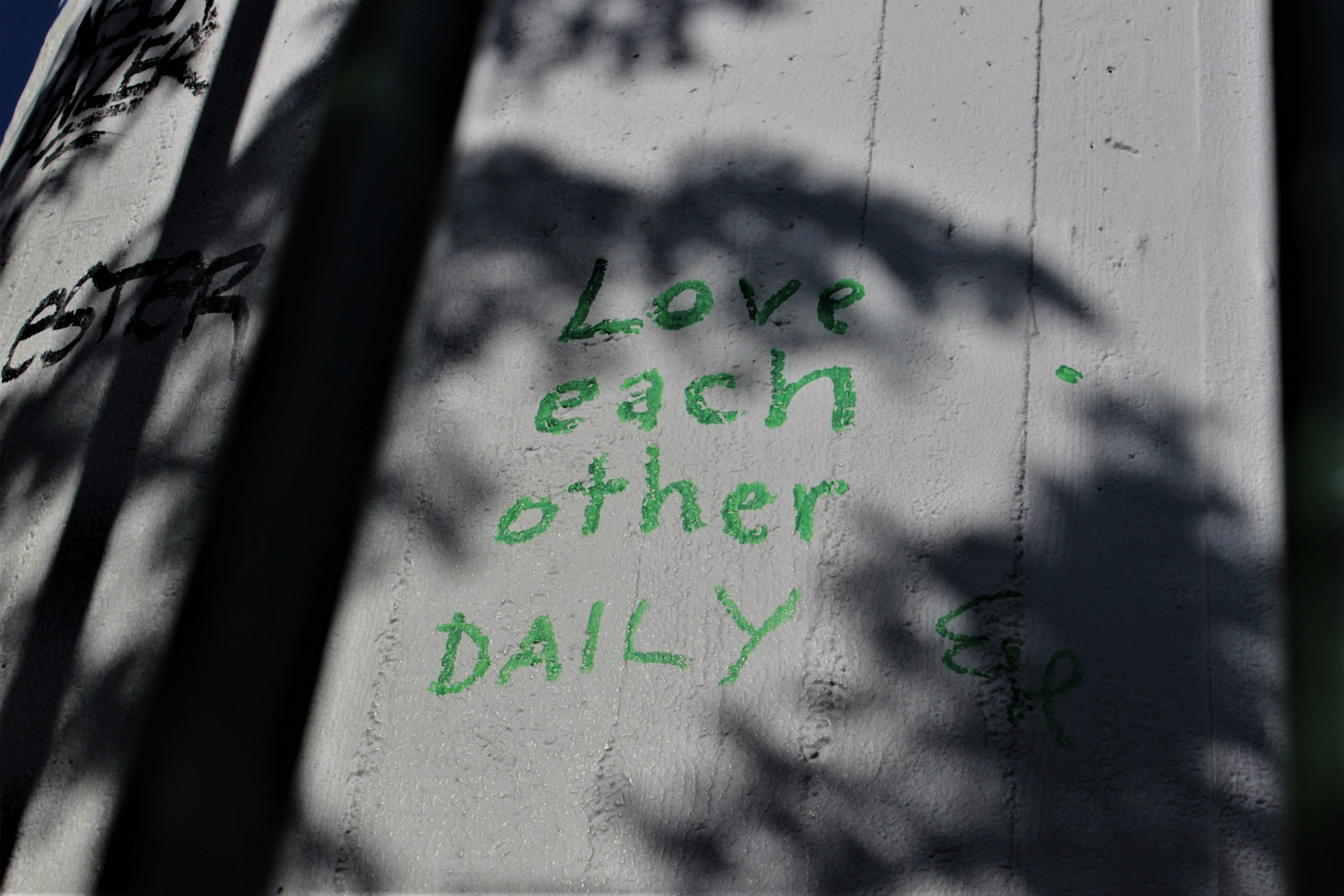 Graffiti on the side of a building that says love each other daily