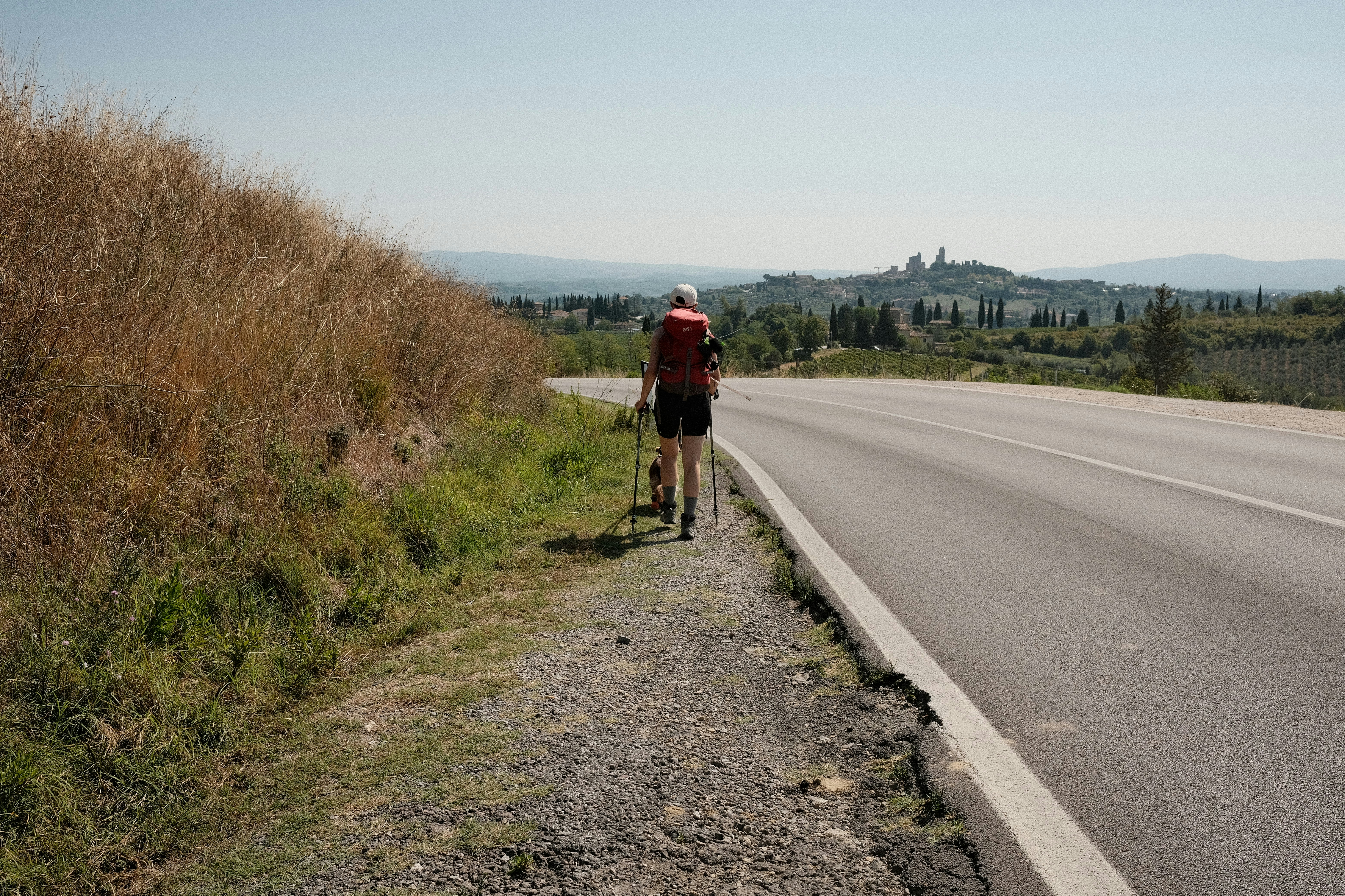 A man riding a bike down a road next to a grass covered hillside