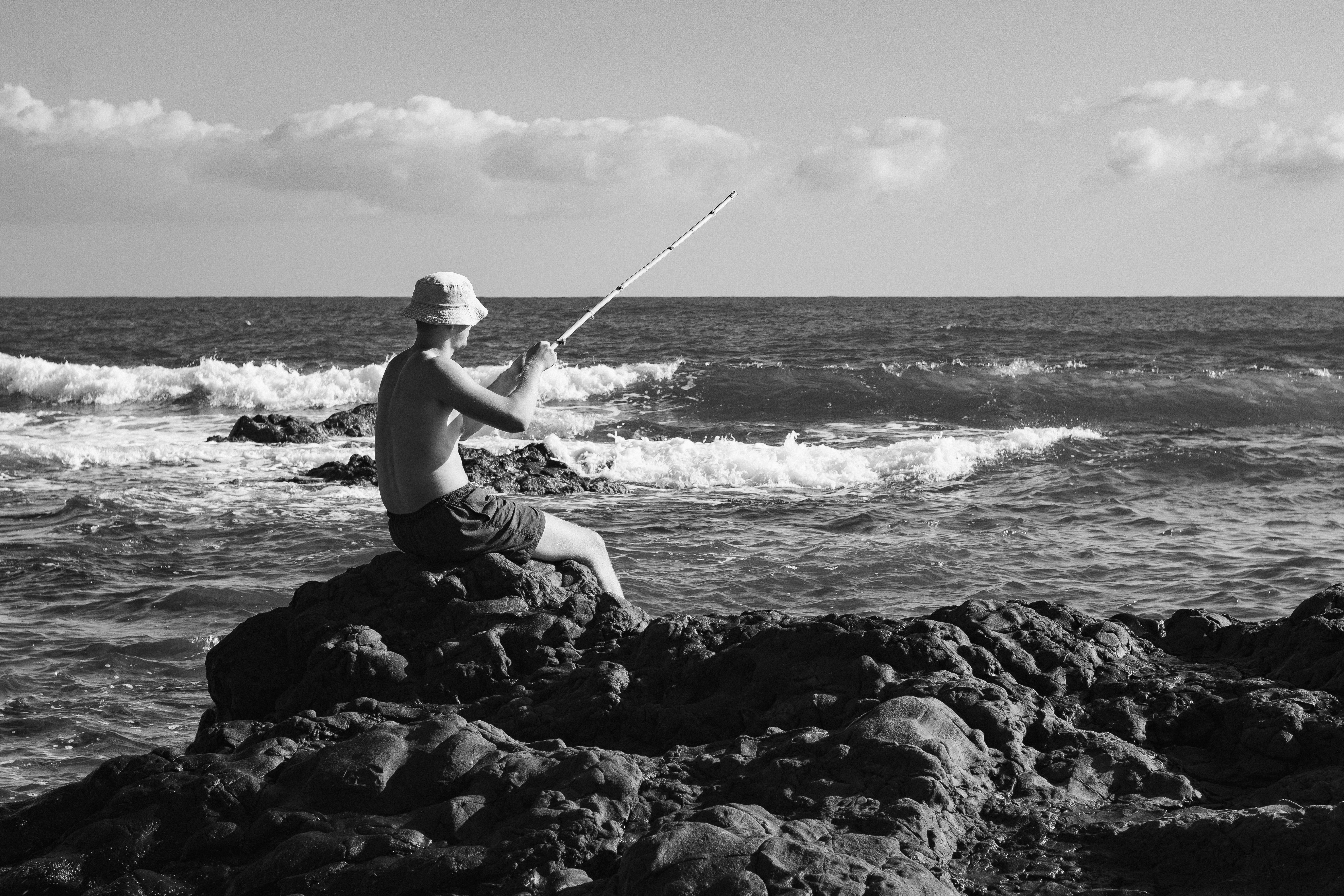 Um homem sentado em uma rocha pescando no oceano