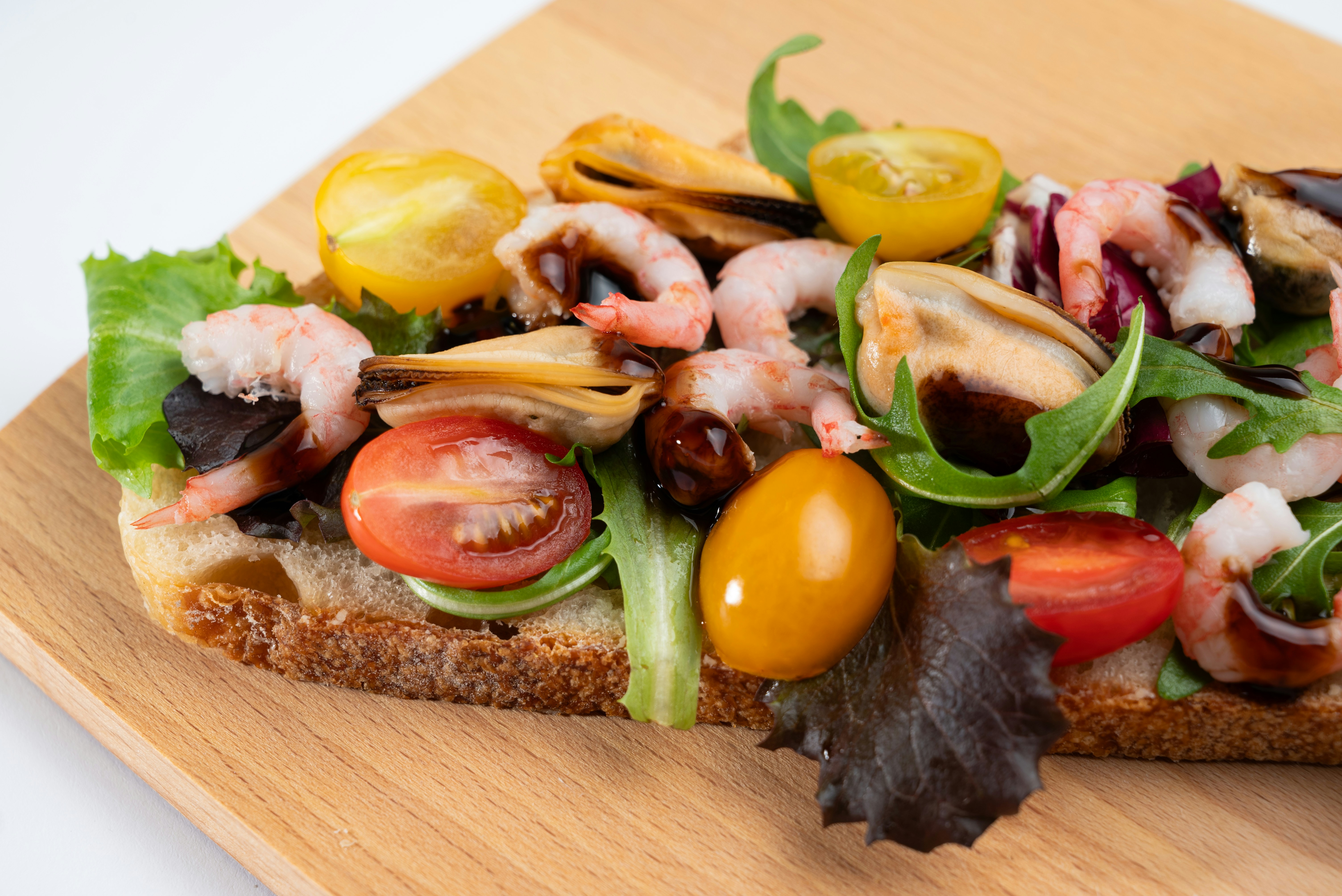 A sandwich with shrimp, tomatoes, and lettuce on a cutting board