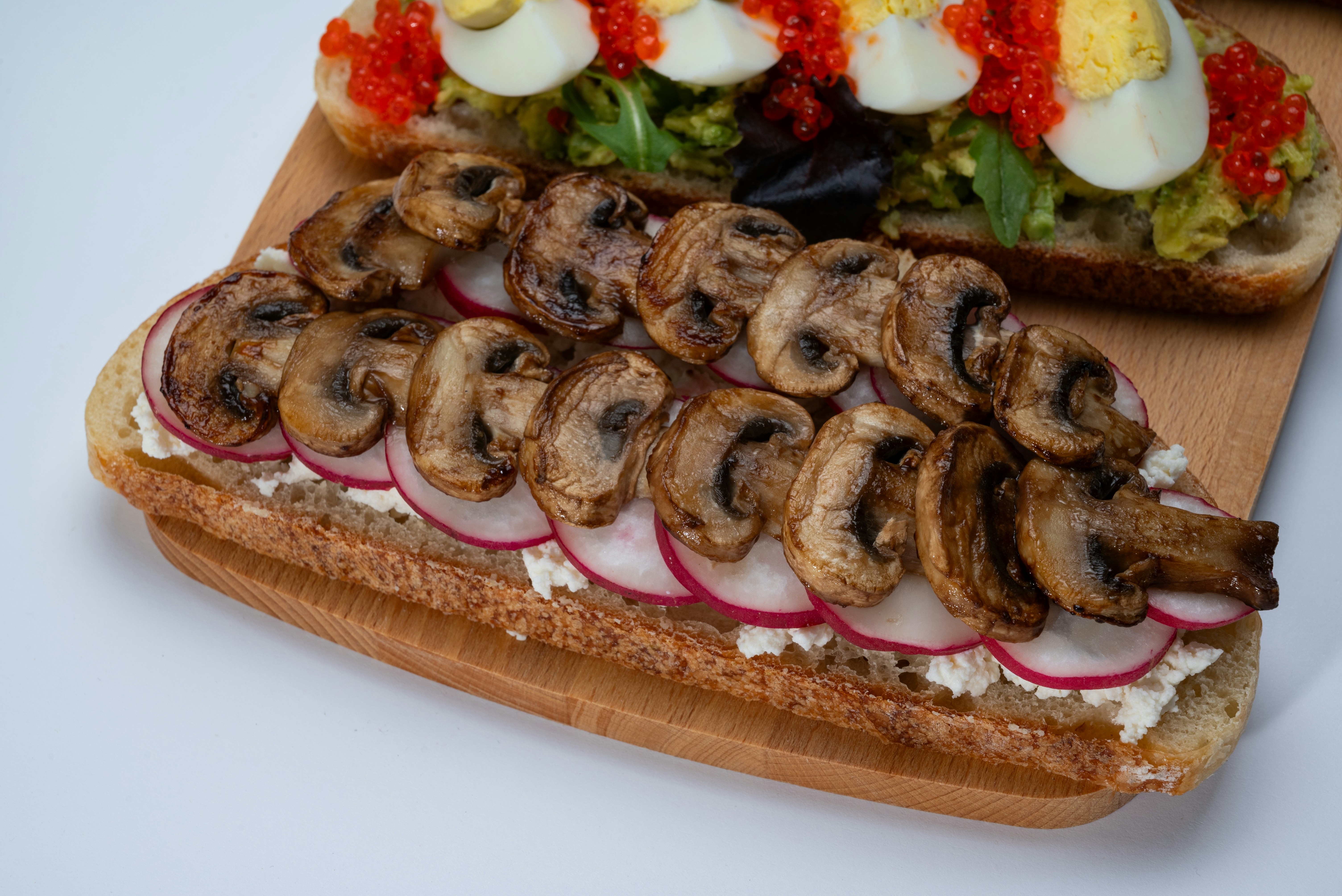 A wooden cutting board topped with a sandwich covered in mushrooms
