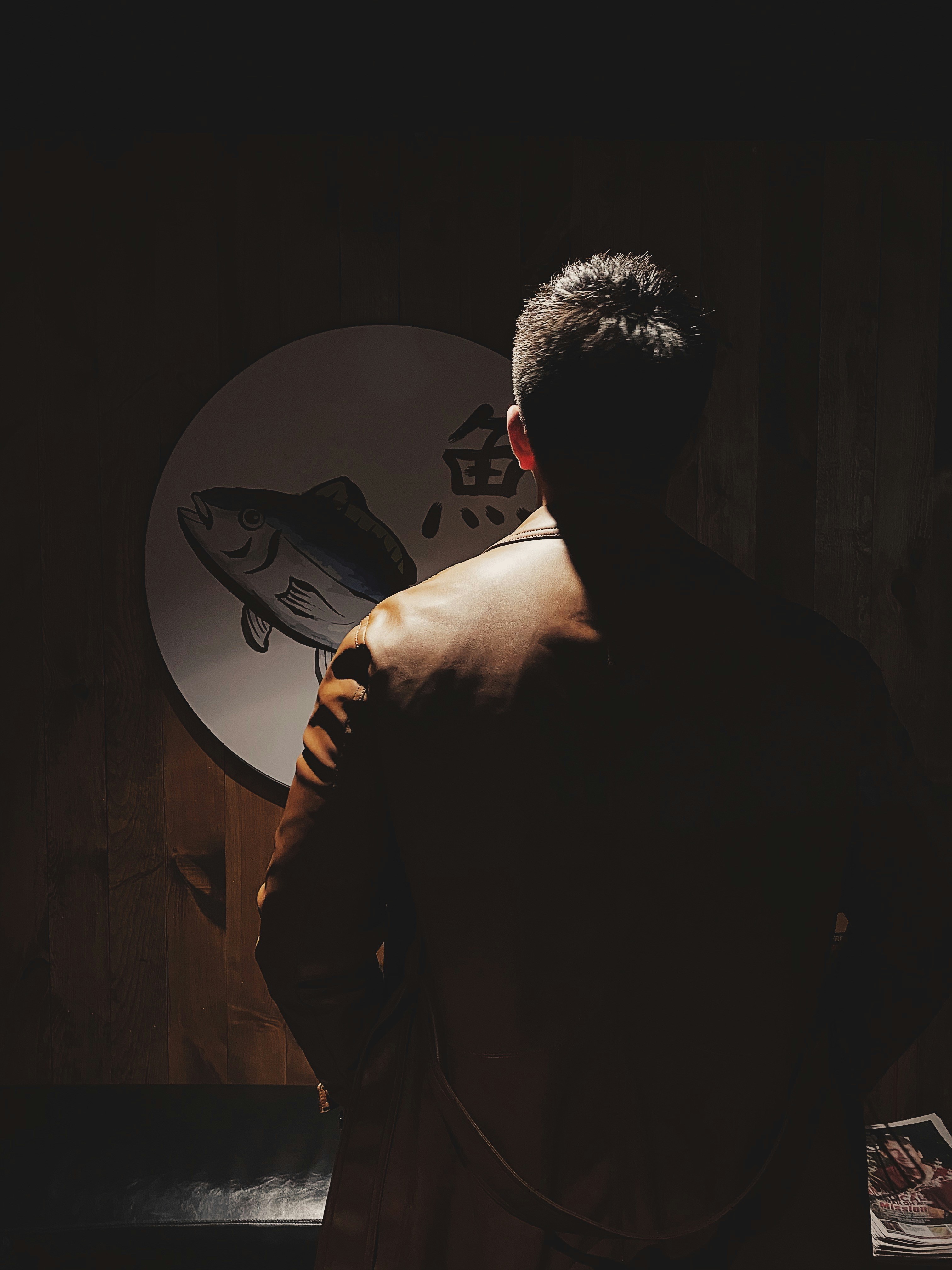 A man standing in a dark room with a fish on the wall