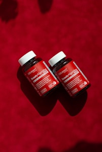 Two bottles of vitamins sitting on a red surface