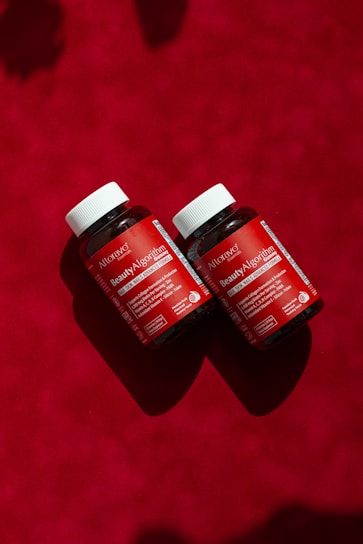 Two bottles of vitamins sitting on a red surface