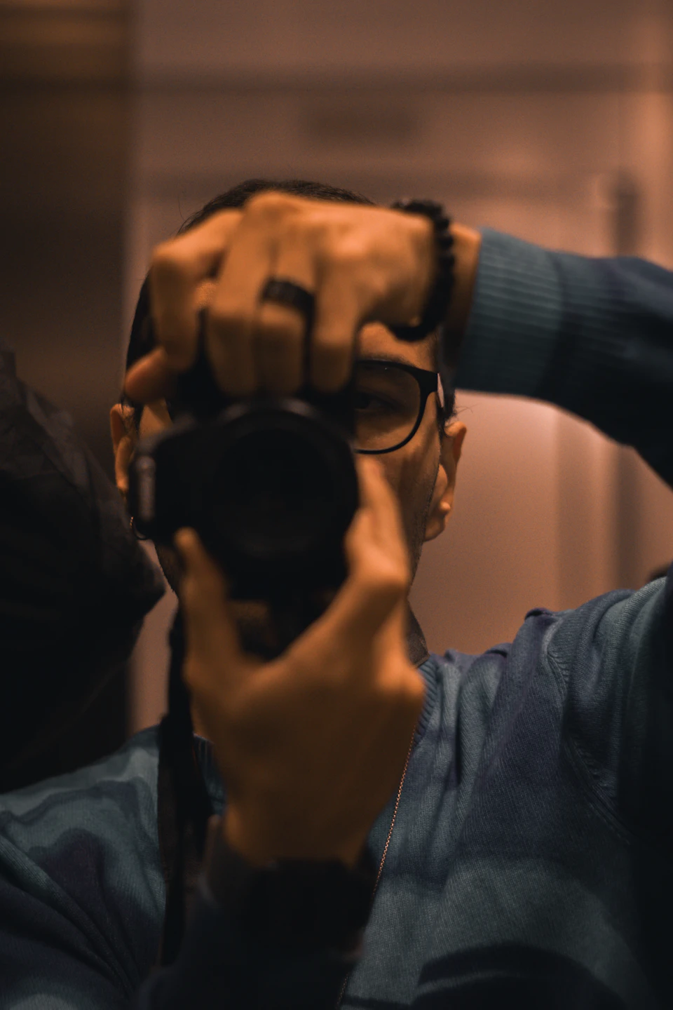 Person holding up face to take selfie with camera around neck and glasses