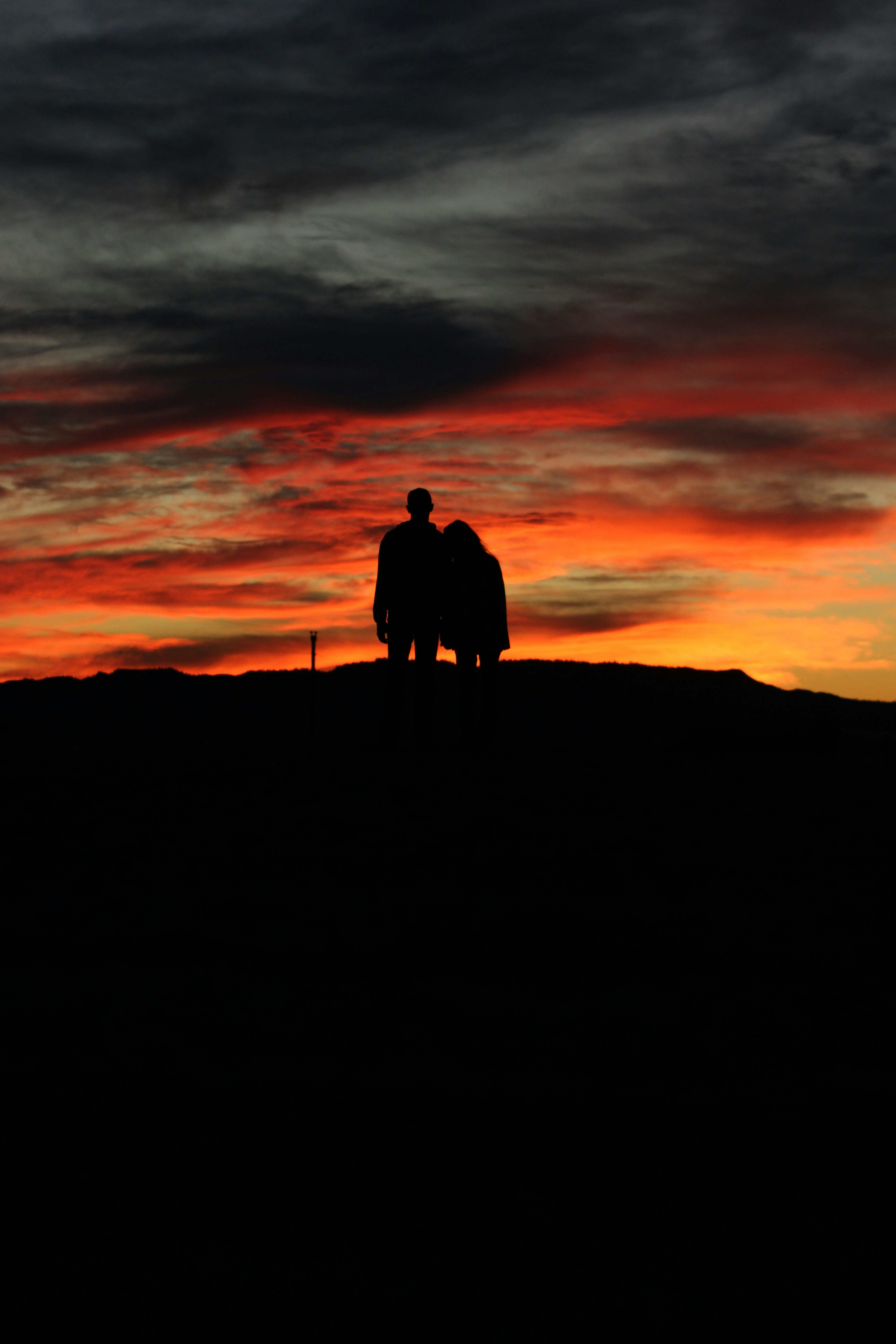 Romantic sunset silhouette of couple on hilltop, dramatic orange and purple sky, peaceful countryside, embracing