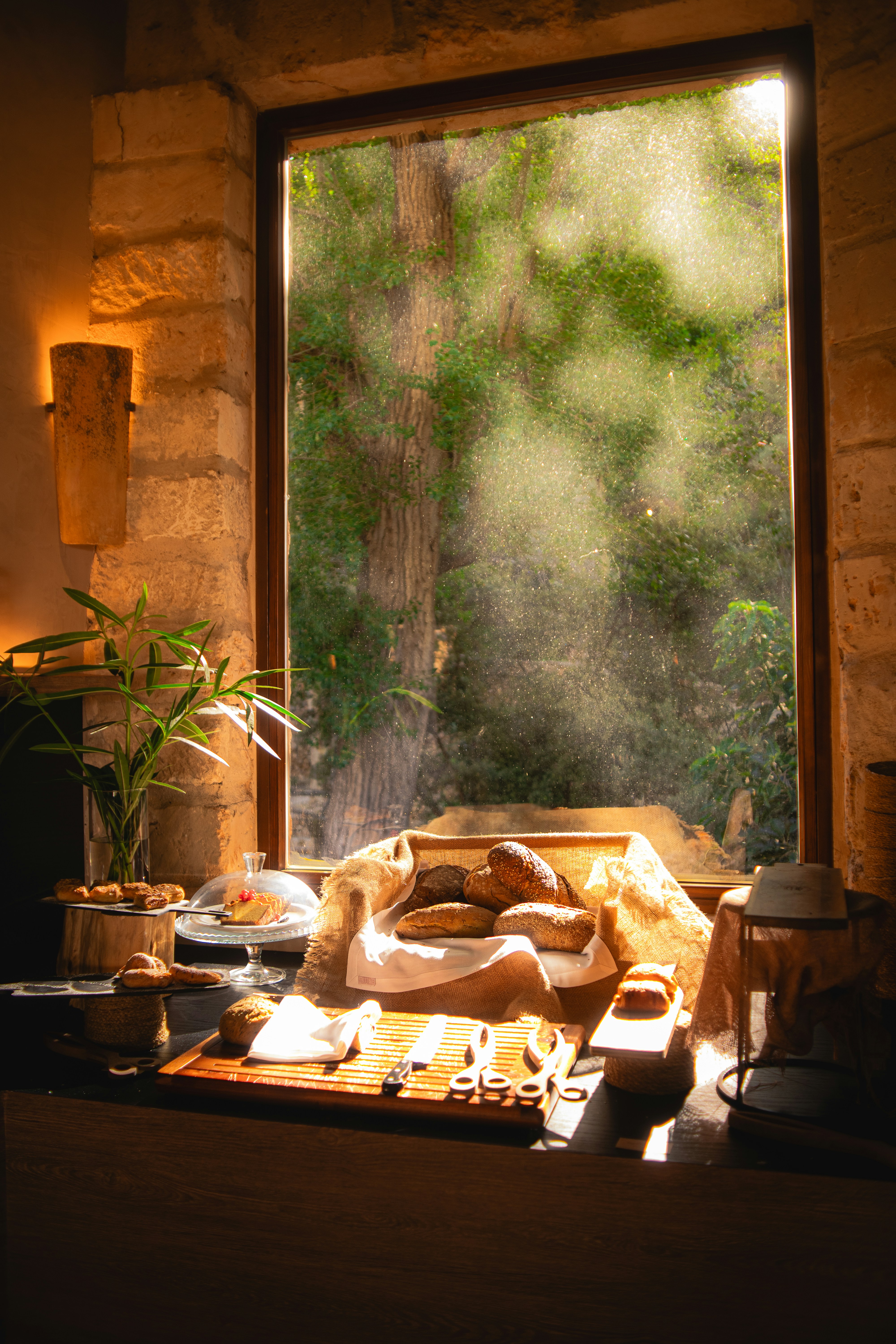 Warm kitchen table with bread and serving pieces beside a sunlit window