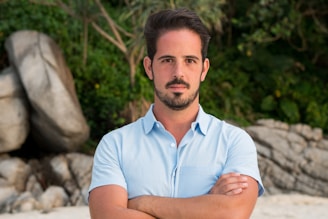 A man standing with his arms crossed on a beach
