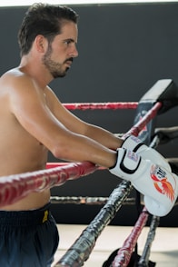 A shirtless man holding a pair of boxing gloves