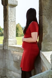 A woman in a red dress leaning against a wall
