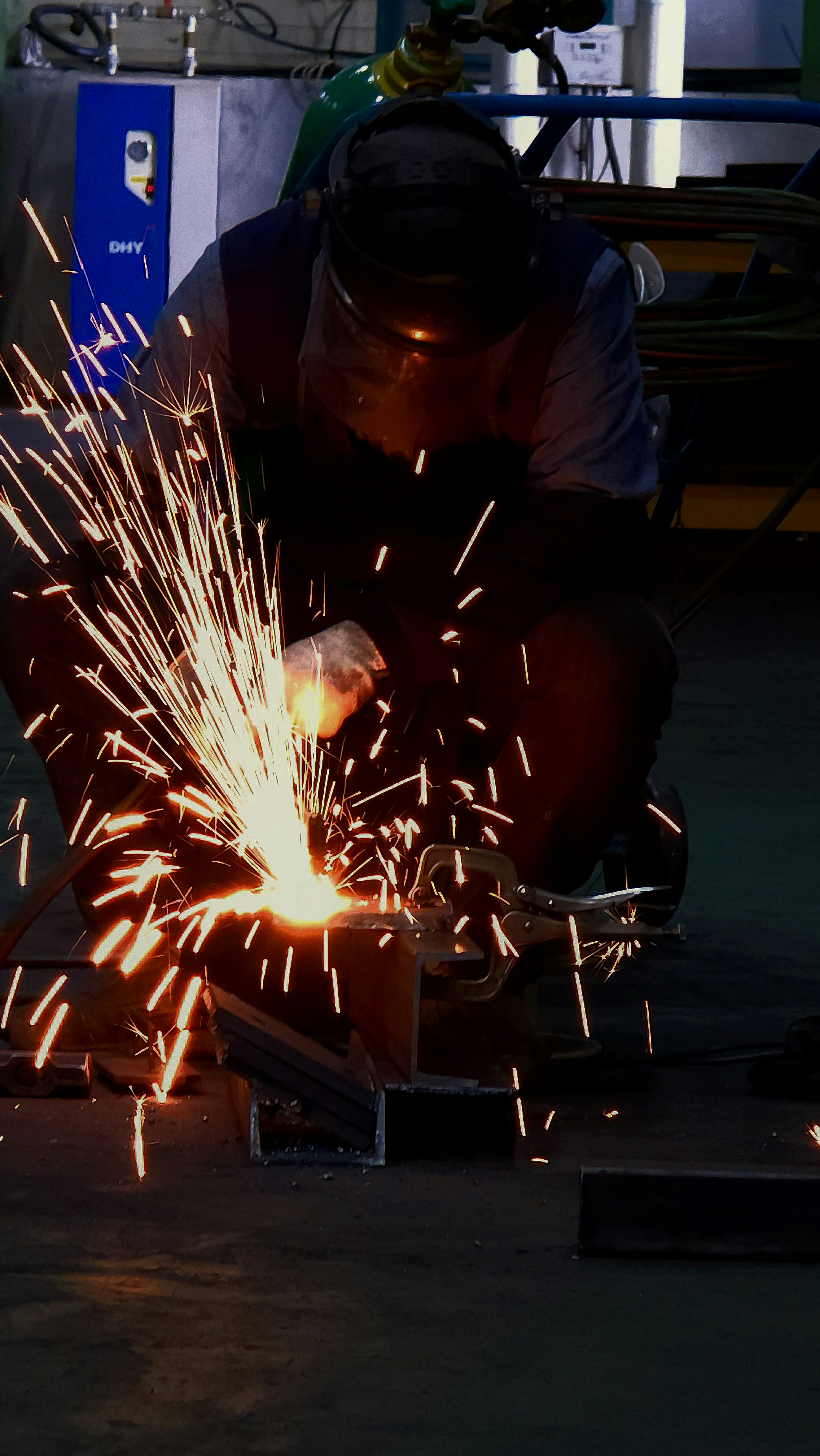 Close-up welding with bright arc flash against very dark metal, industrial welder in protective gear
