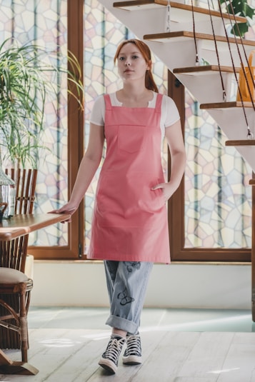 A woman in a pink apron standing in front of a staircase