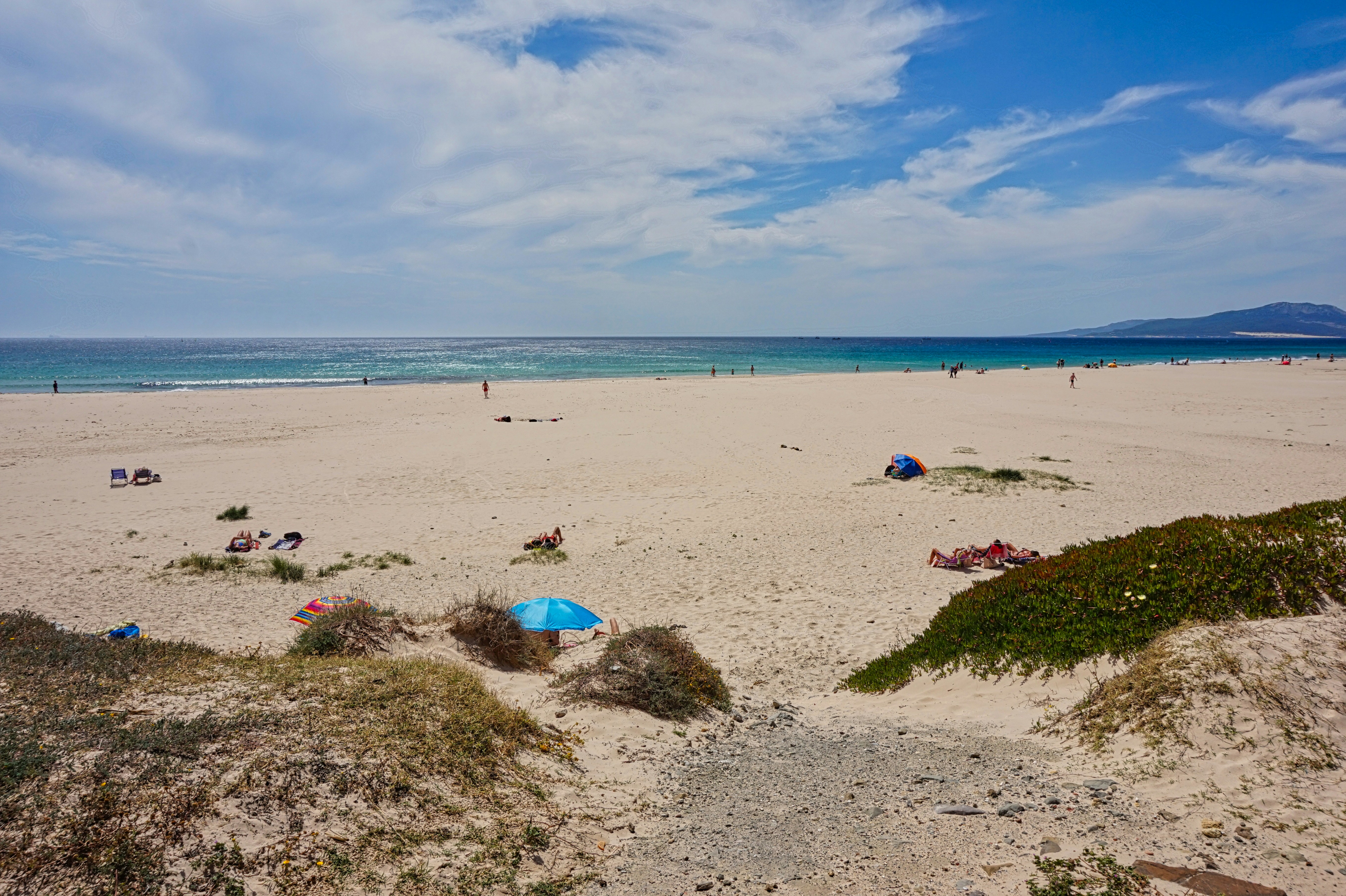 A sandy beach with blue umbrellas and people in the water