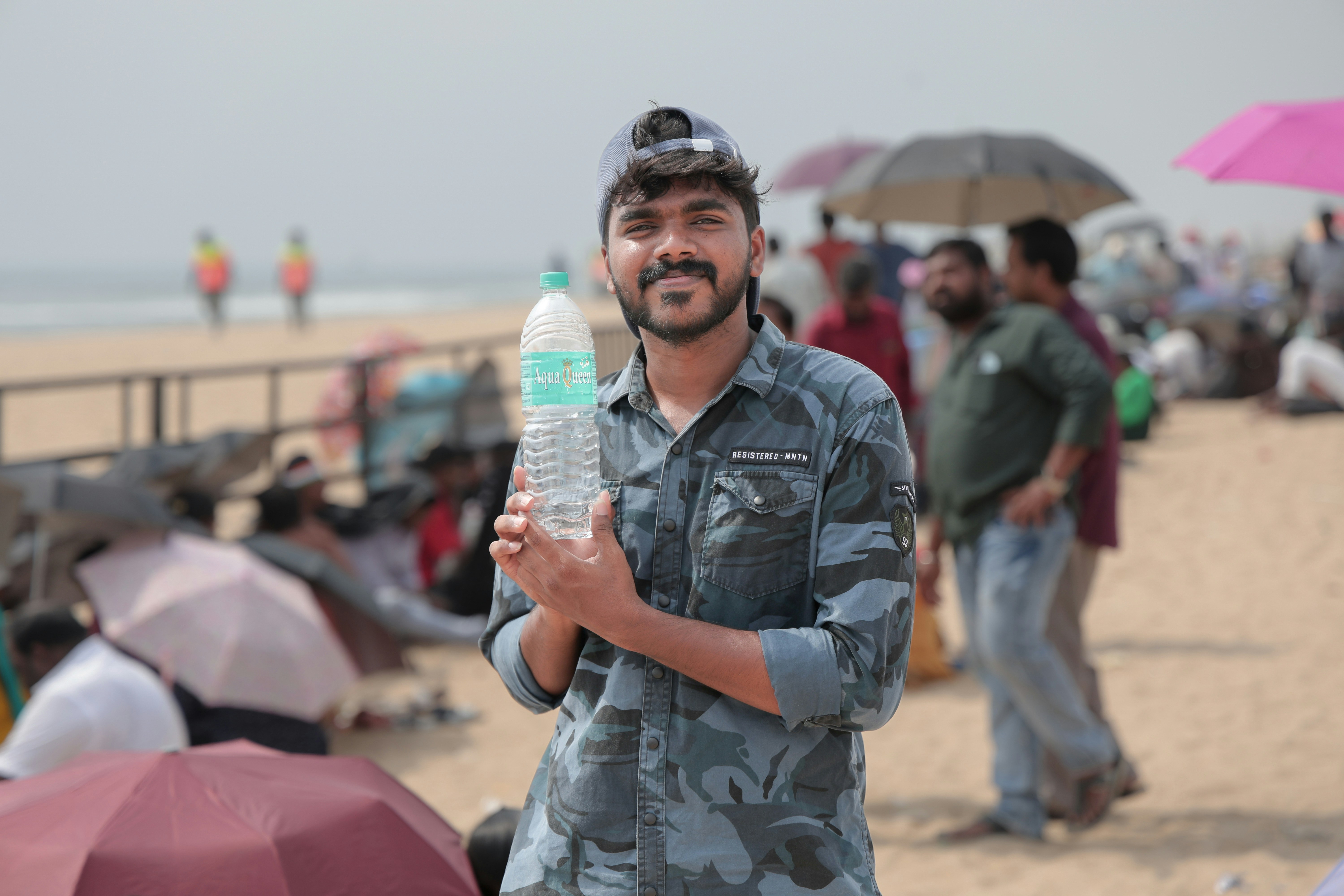 A man standing on a beach holding a bottle of water