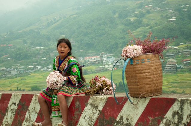 A woman sitting on a wall with a basket of flowers