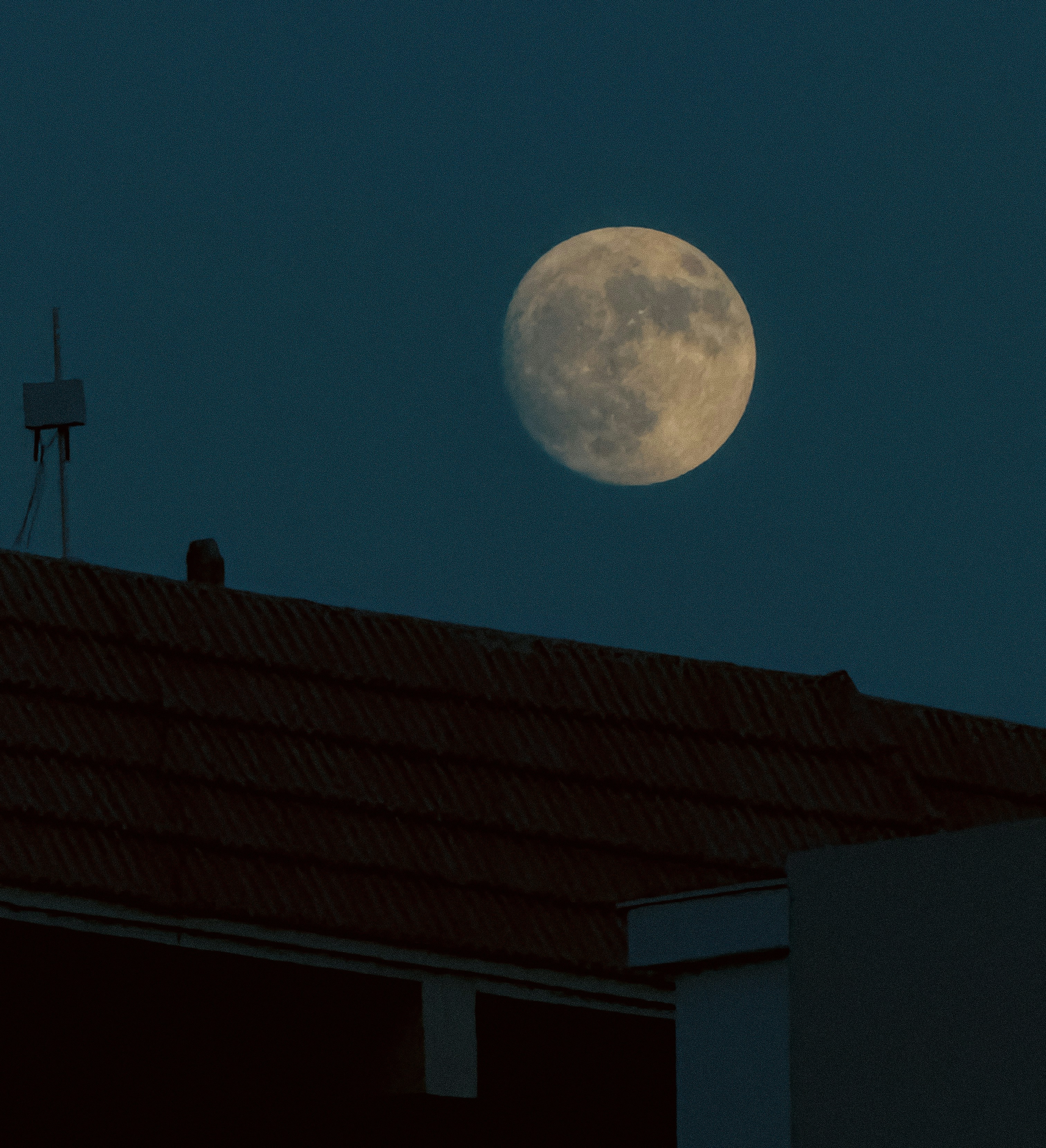 Una luna piena è vista sopra un tetto