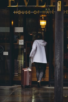 A woman walking out of a building with a suitcase