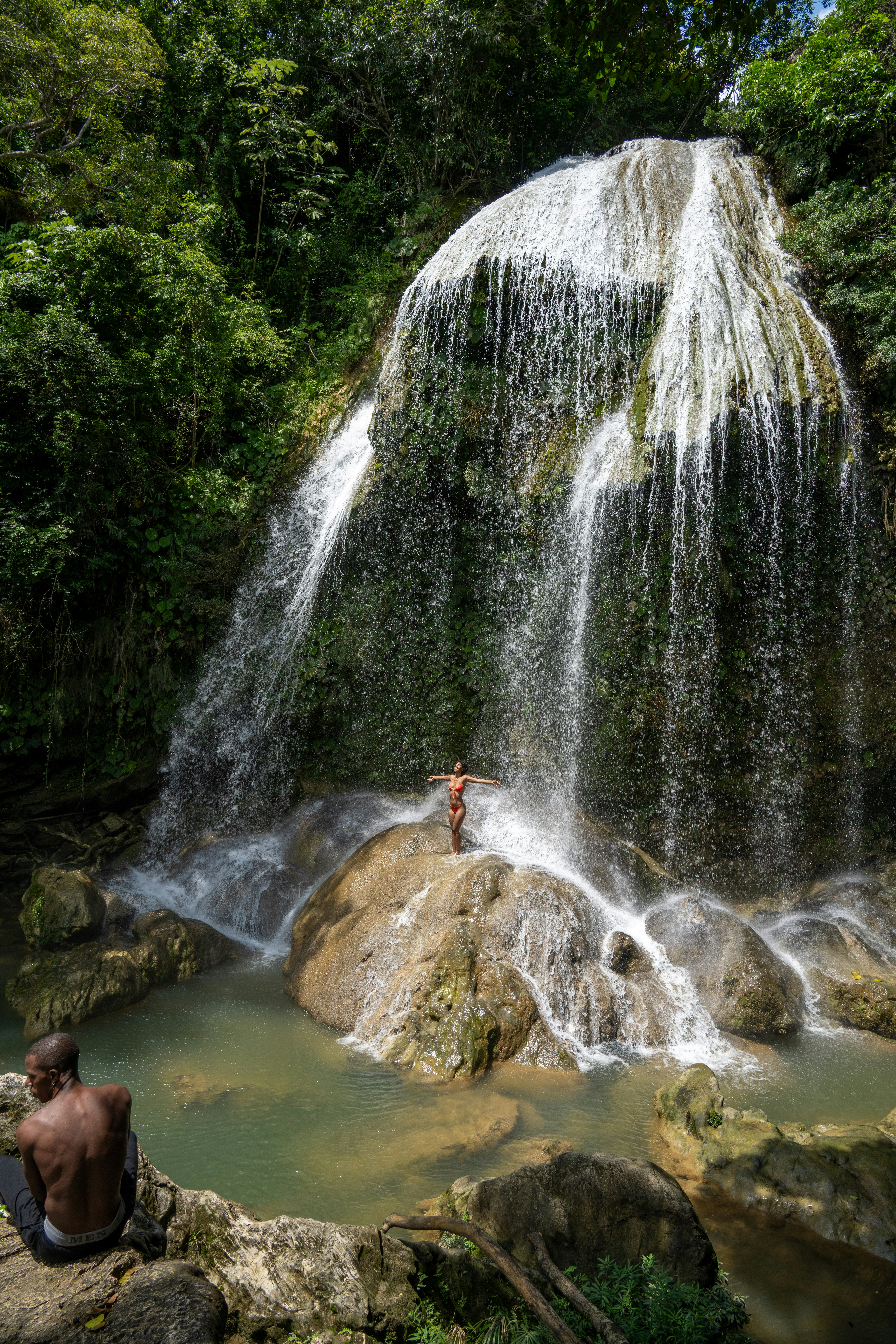 Ein Mann sitzt auf einem Felsen vor einem Wasserfall