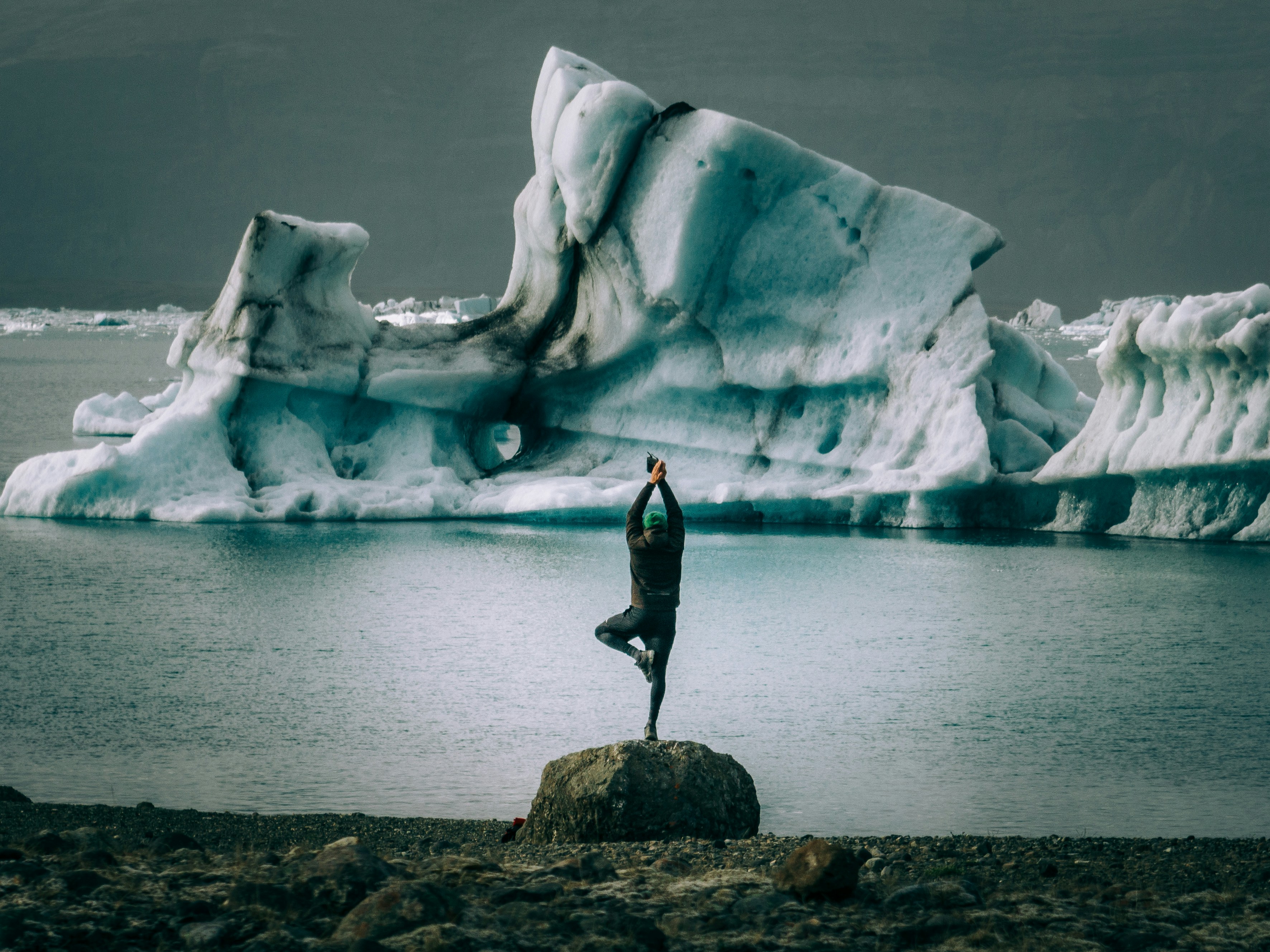 A person standing on a rock in front of an iceberg