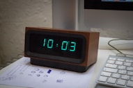 A digital clock sitting on top of a desk next to a keyboard