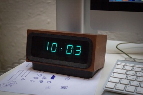 A digital clock sitting on top of a desk next to a keyboard