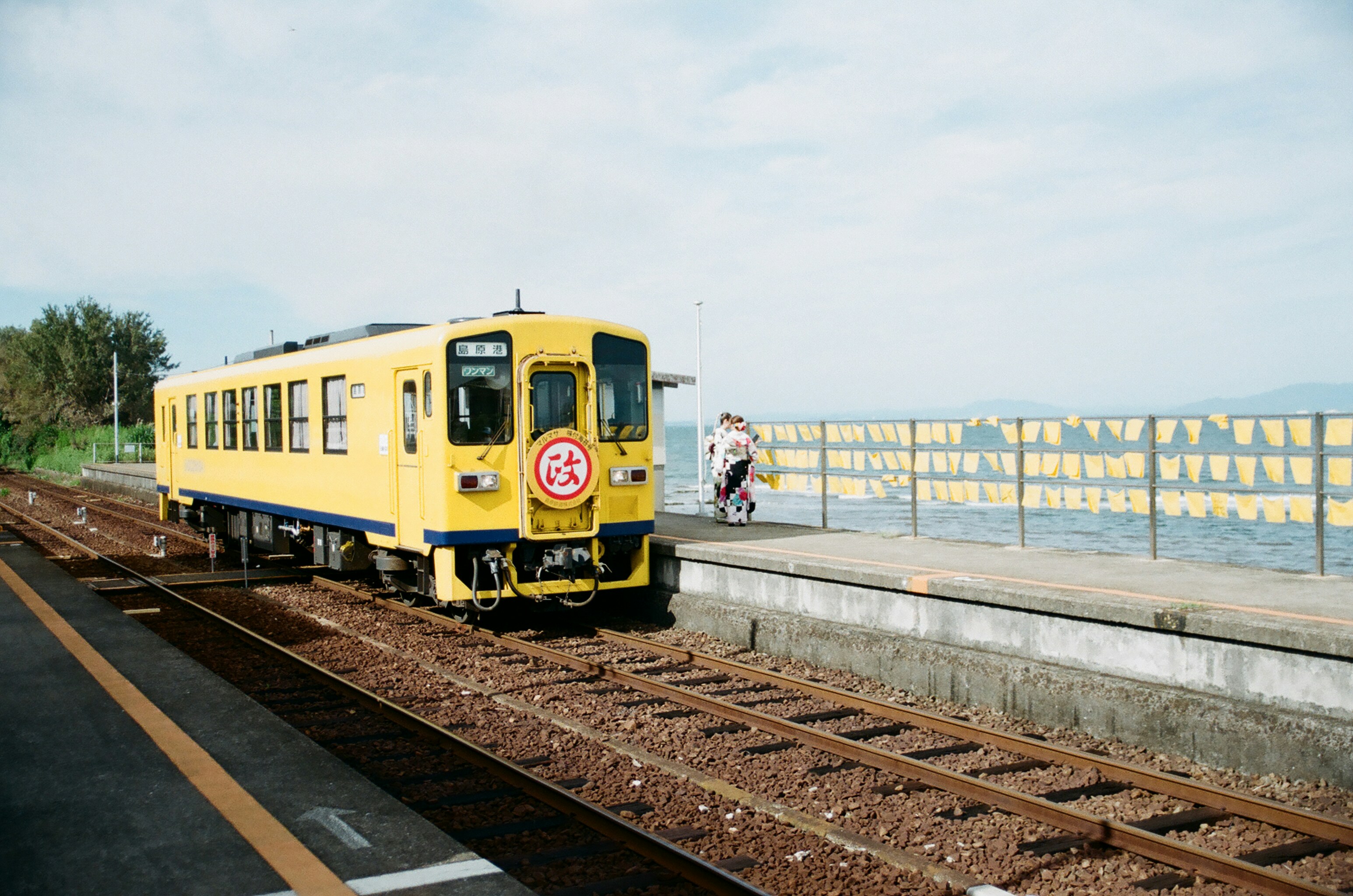 A yellow train traveling down train tracks next to a body of water