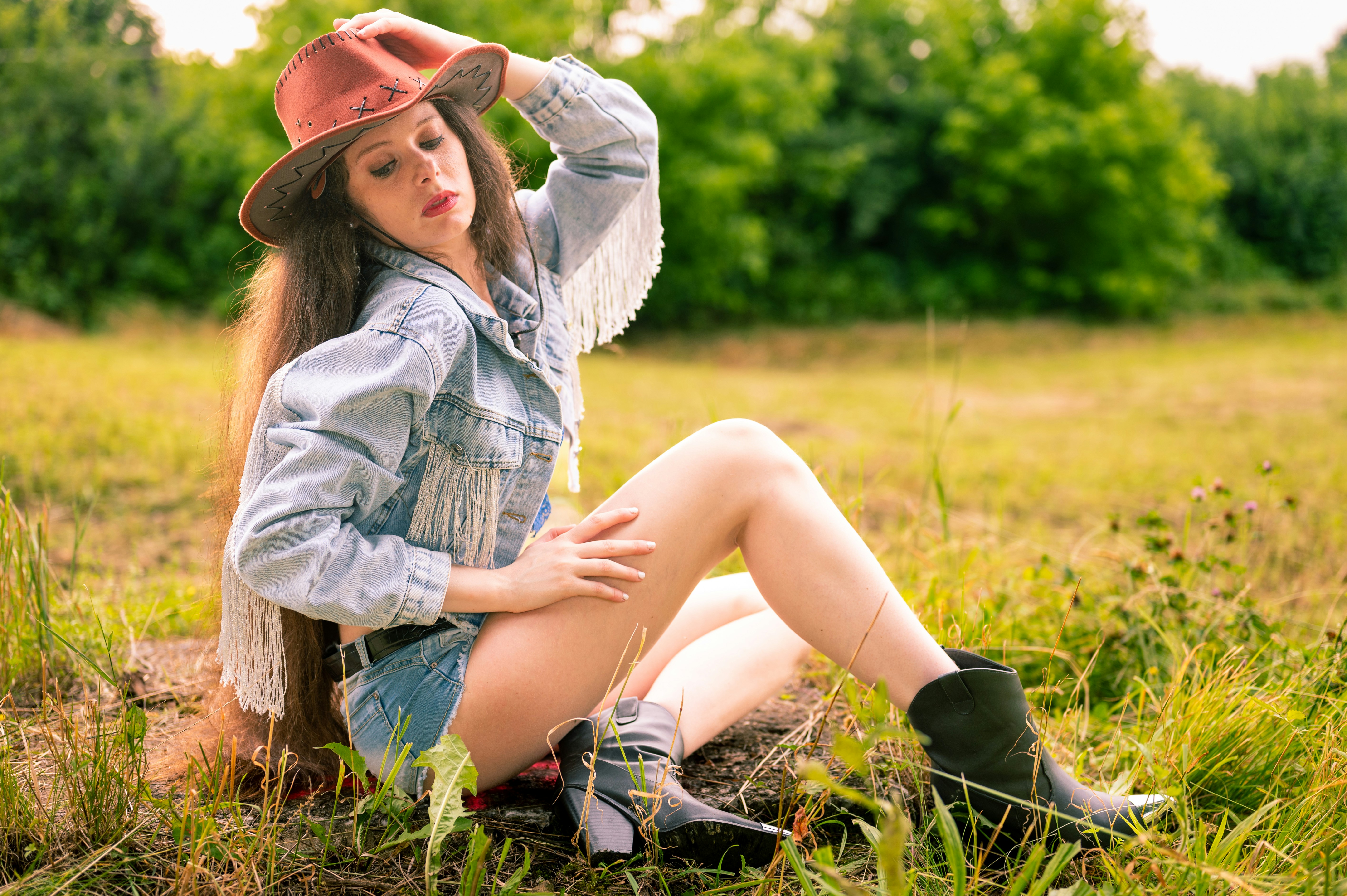 A woman sitting in the grass wearing a hat