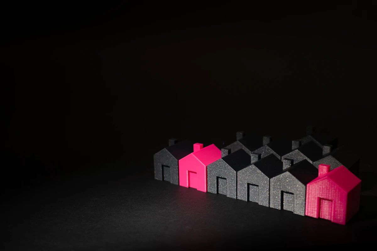 A row of small grey model houses on a dark table, two of them pink