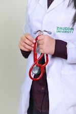 A woman in a white lab coat holding a red stethoscope