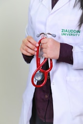 A woman in a white lab coat holding a red stethoscope