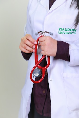 A woman in a white lab coat holding a red stethoscope