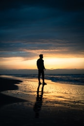 A man standing on top of a beach next to the ocean